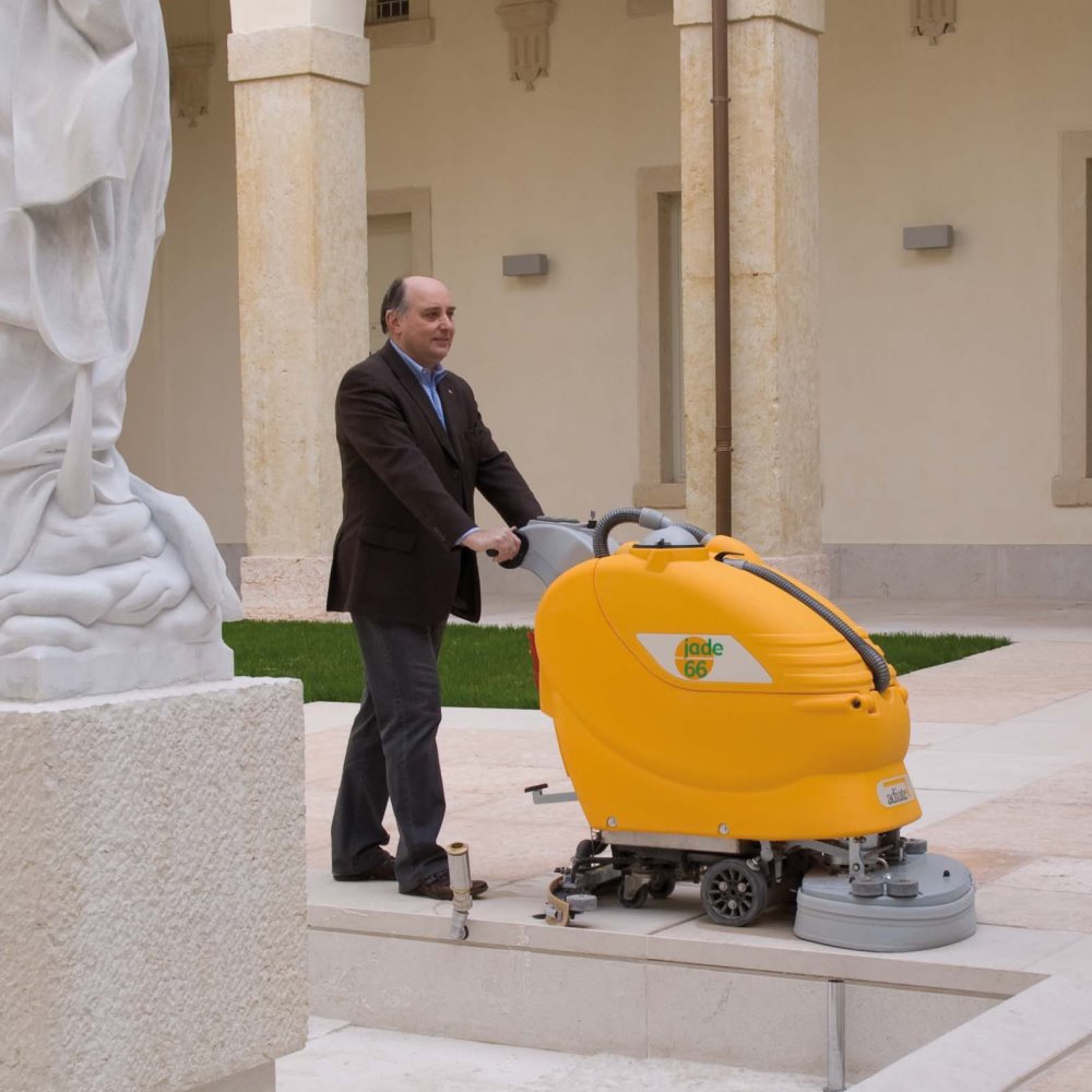 Man operating a yellow Adiatek Jade 66 Auto floor cleaning machine in front of a statue