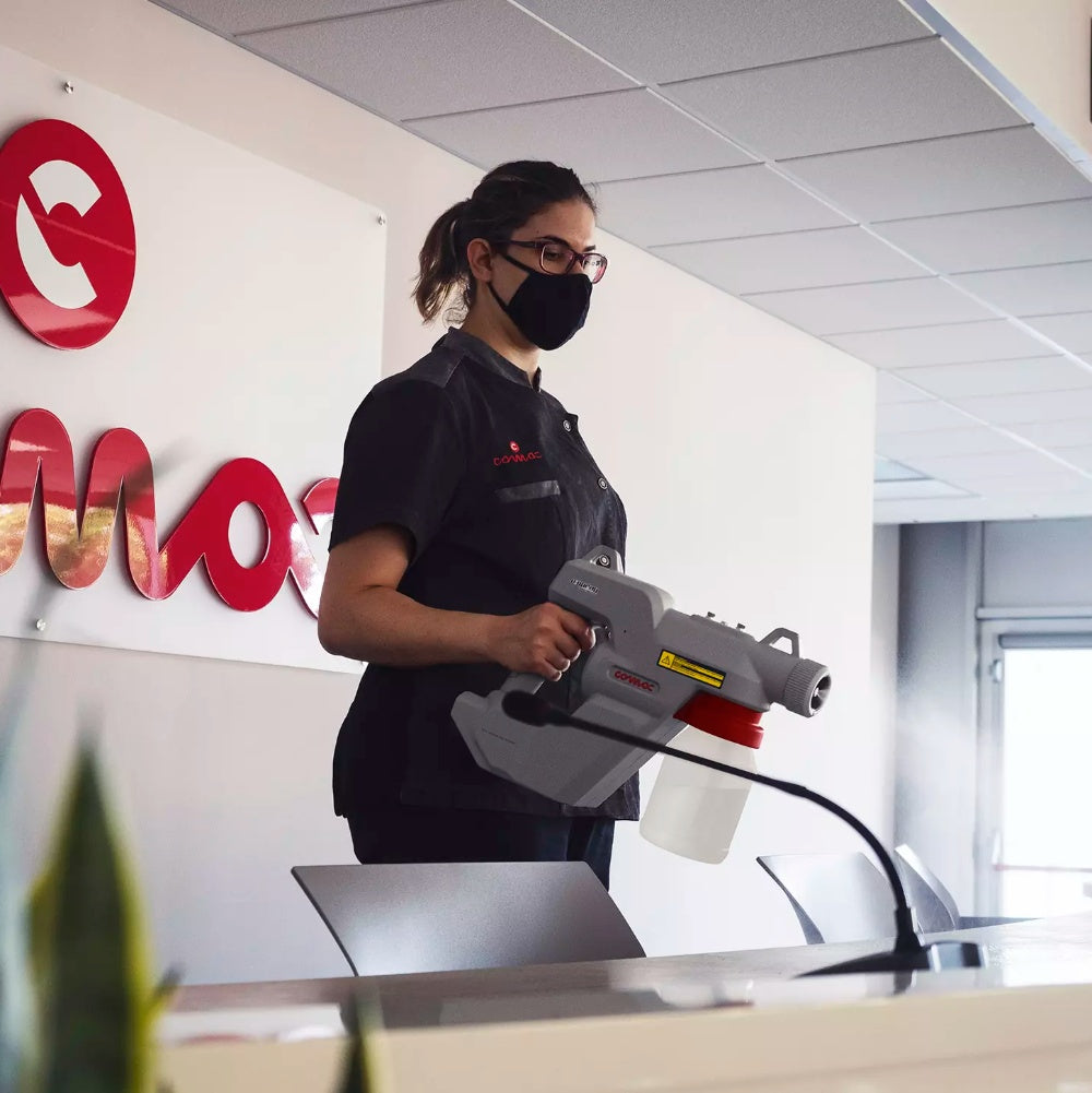 Person in a black uniform using a Comac Electrostatic E-Spray in an office setting.