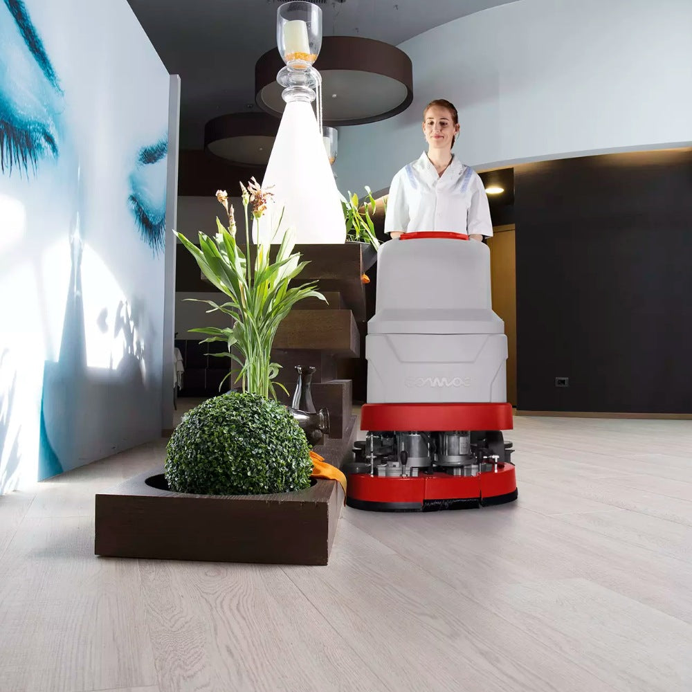 Person operating a floor cleaning machine in a modern indoor setting with plants and decor.