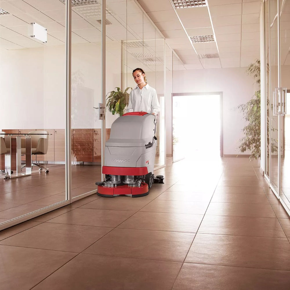Person operating a floor cleaning machine in a modern office setting