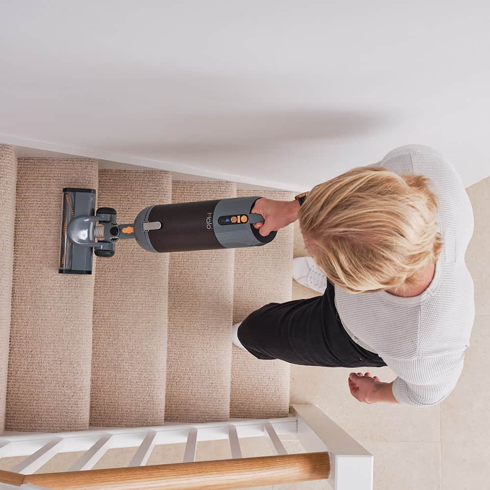Person using a Halo Capsule Stick Vacuum Cleaner on a carpeted staircase.