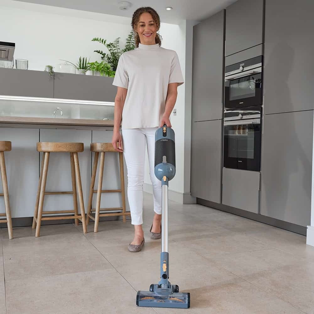 Person holding a Halo Capsule Stick Vacuum Cleaner in a modern kitchen.