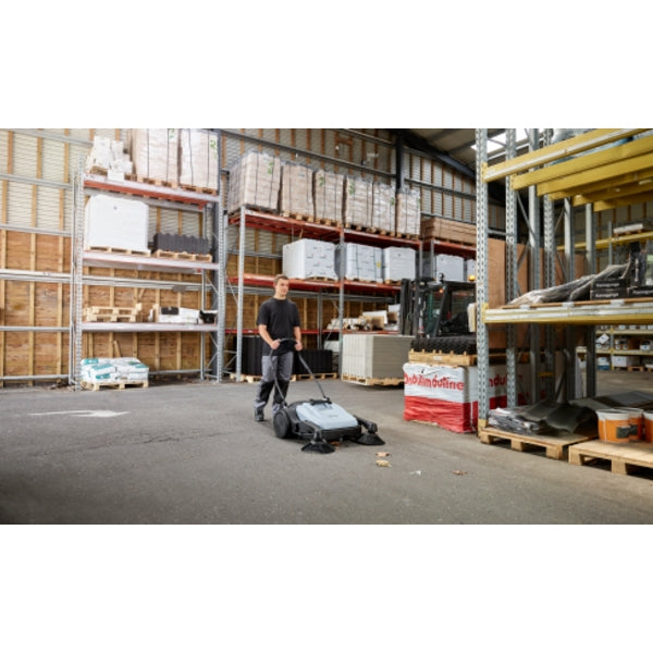 Person operating a Nilfisk SW250 Walk Behind Sweeper in a warehouse setting