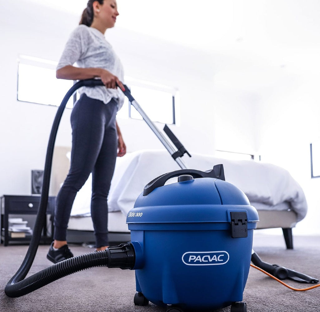 Person using a blue PacVac vacuum cleaner in a room with furniture
