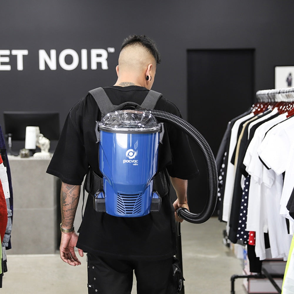Person wearing a blue backpack vacuum cleaner in a clothing store.