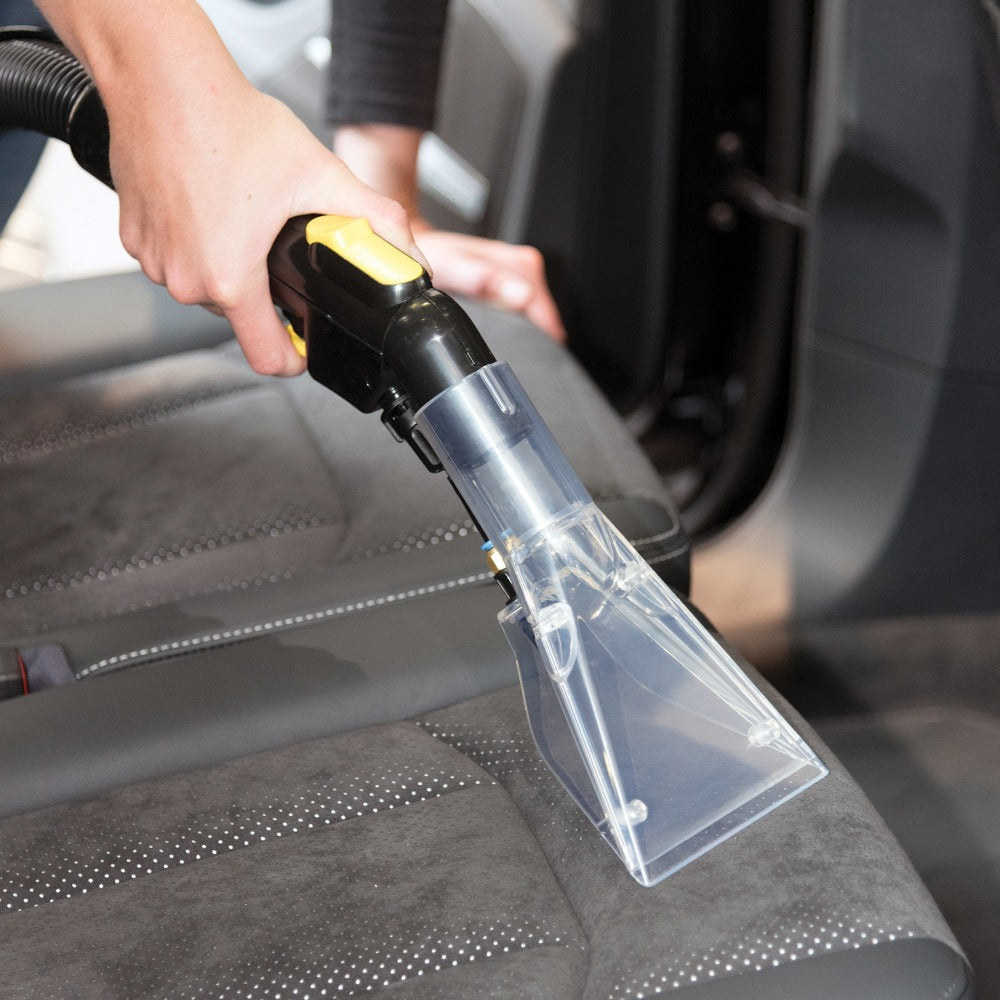 Person cleaning car interior with a handheld vacuum cleaner.