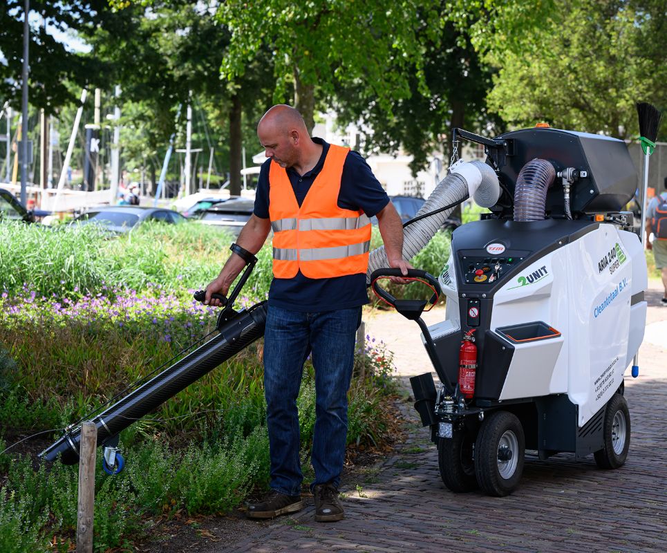 Man operating a small piece of gardening equipment on a path with trees and cars in the background