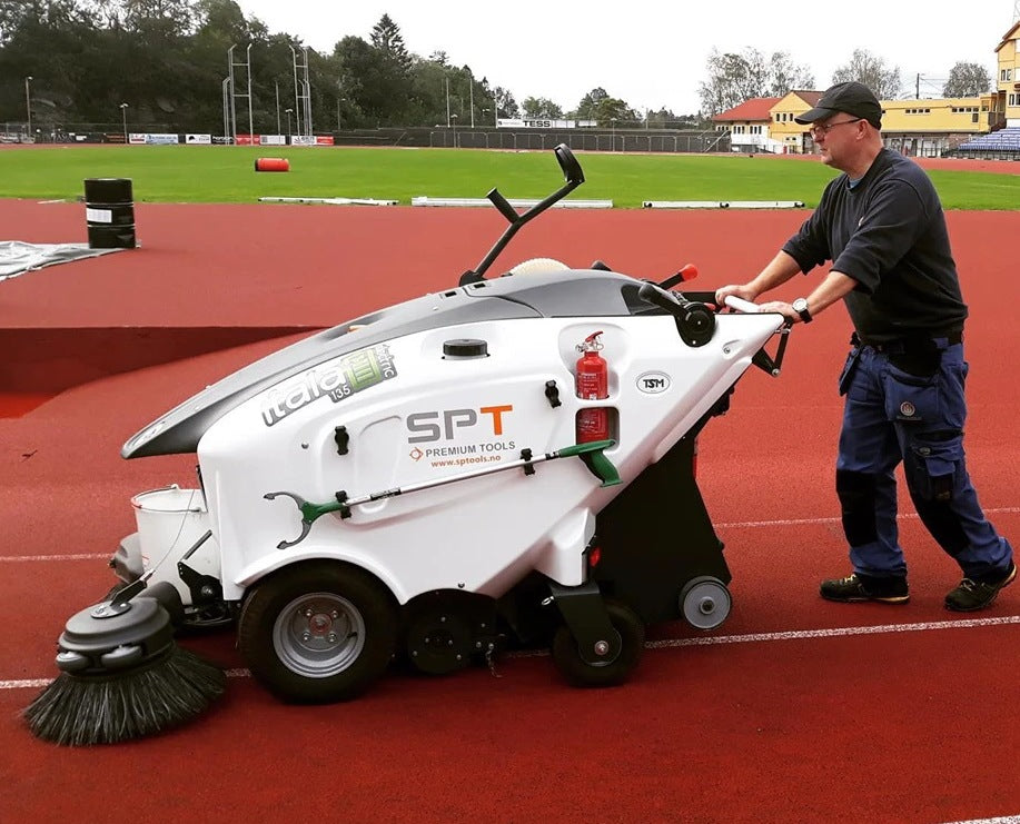 Person operating a large cleaning machine on a sports field