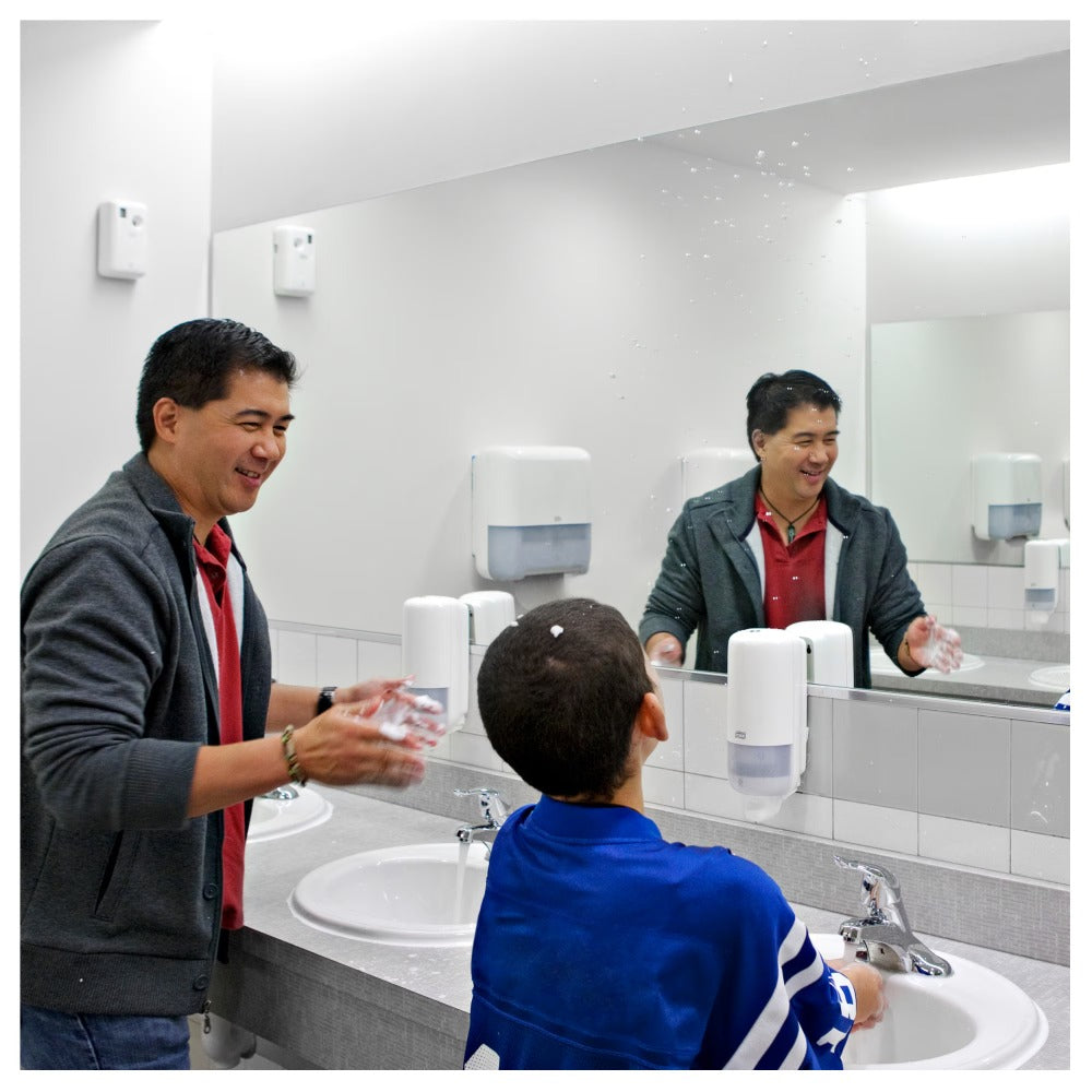 Man and child washing hands in a bathroom with soap dispensers and mirrors.