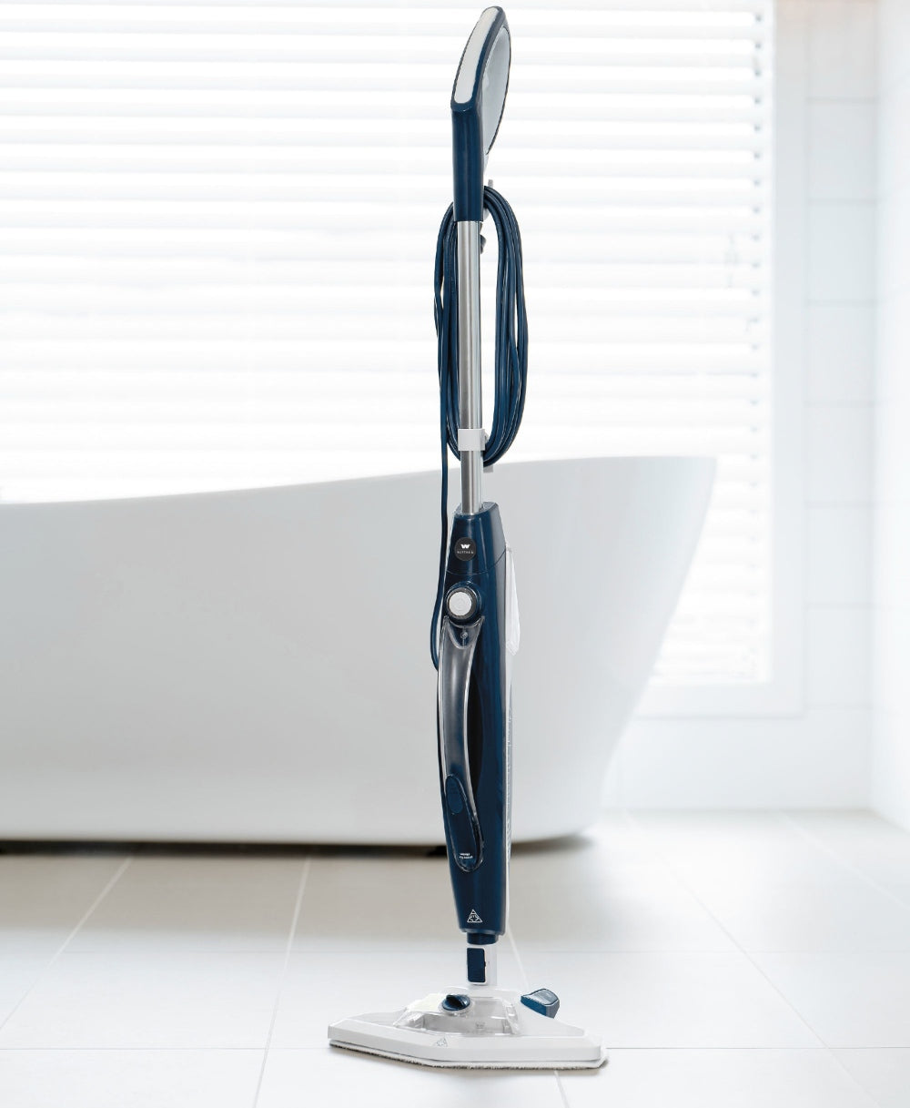 Blue and silver Wertheim Dual Steam Mop Plus on a white floor with a white wall and window blinds in the background.