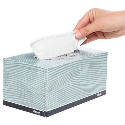 Hand pulling a tissue from a Kleenex box on a white background