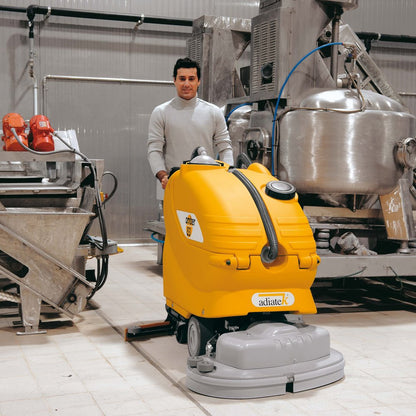 Person operating a yellow Adiatek Amber 83 Auto Scrubber floor cleaning machine in an industrial setting