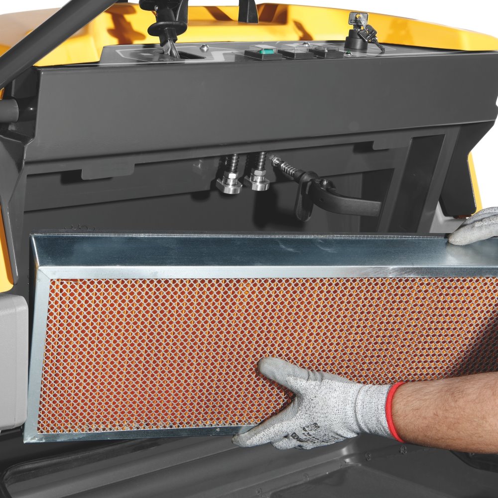 Person wearing a glove holding a metal air filter in front of a vehicle's engine bay.