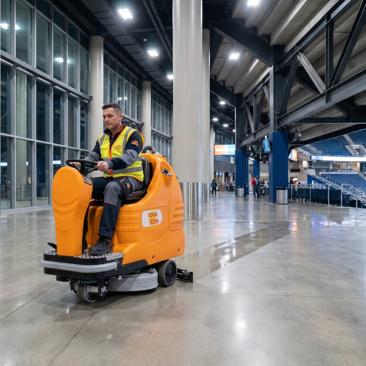 Person operating a large orange cleaning machine in a large indoor area with high ceilings.