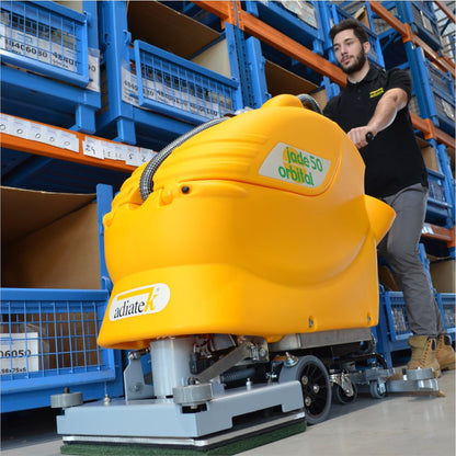 Person operating a yellow Adiatek Jade 50 Orbital floor cleaning machine in a warehouse setting