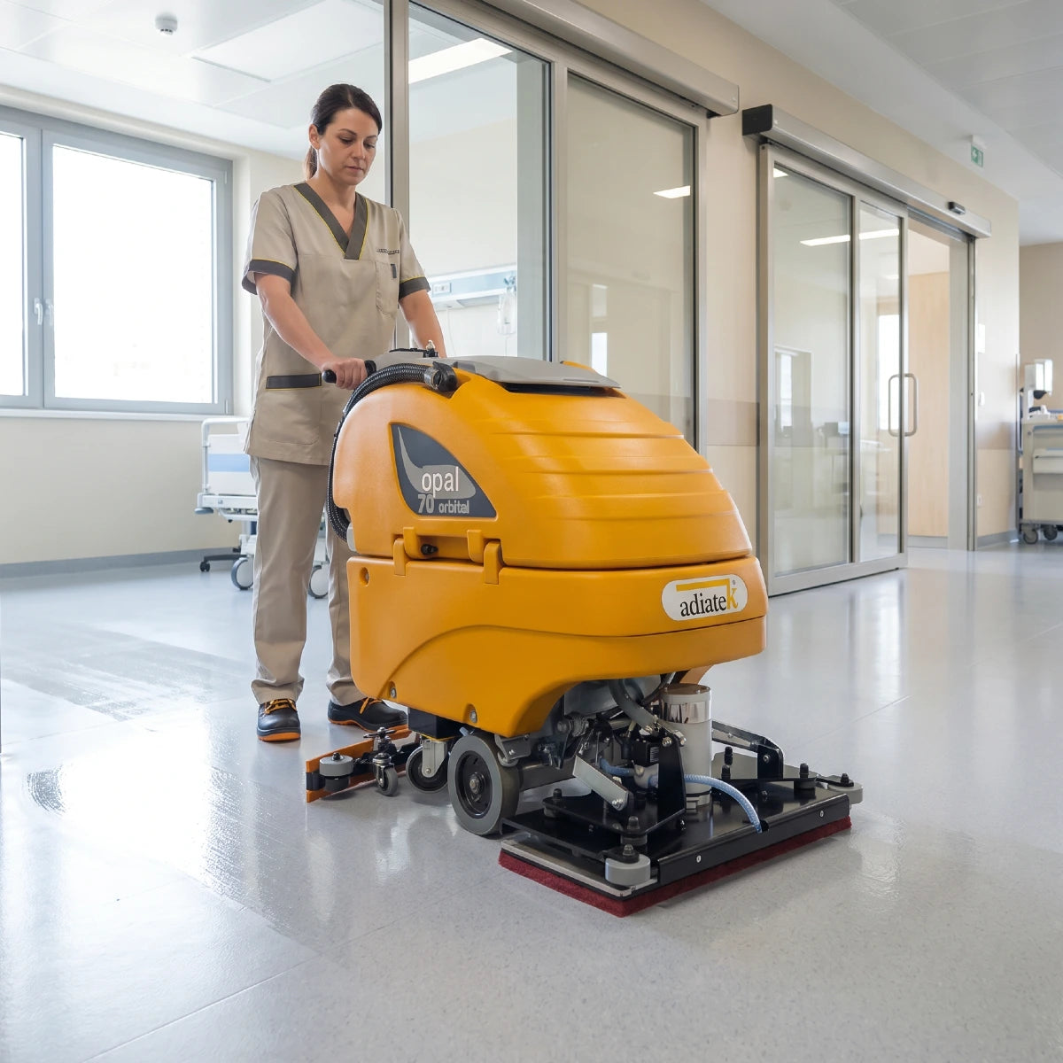 Person operating a yellow floor cleaning machine in a modern hospital building.