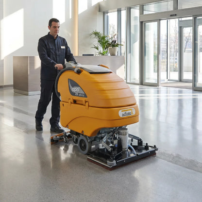 Person operating a large floor cleaning machine in a modern building foyer.
