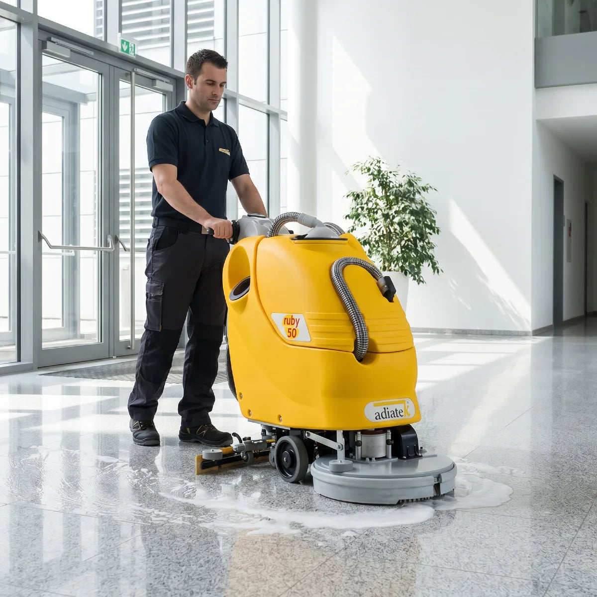 Person operating a yellow floor cleaning machine in a modern building.