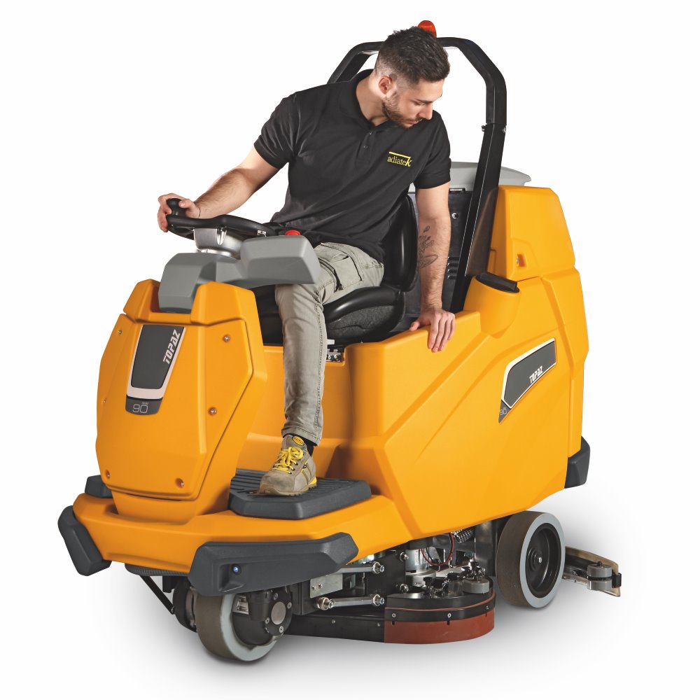 Person operating a yellow Adiatek Topaz 90 Ride On Auto Scrubber floor cleaning machine on a white background