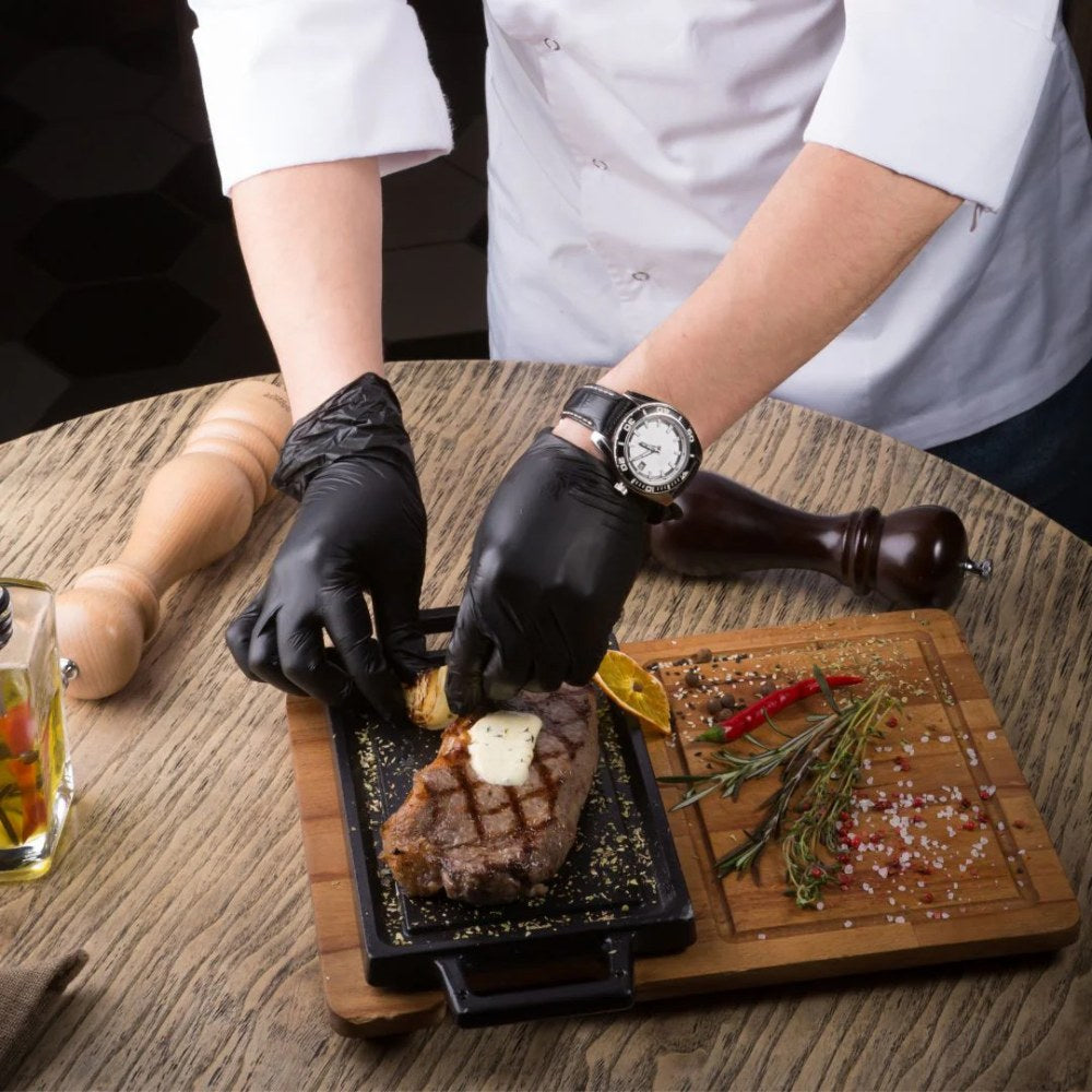 Person seasoning a steak with black nitro gloves on a wooden table