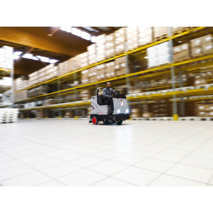 Person driving a Comac C85 Essential Scrubber in a warehouse setting