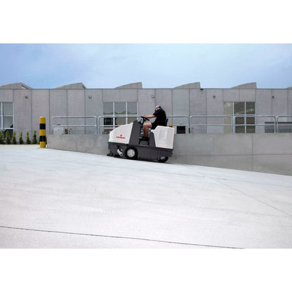 Person operating a Comac CS110B  Sweeper ride-on floor cleaning machine in front of a building