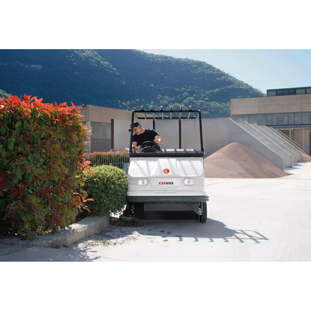 Person driving a Comac CS120B Ride On Sweeper on a sunny day with mountains in the background