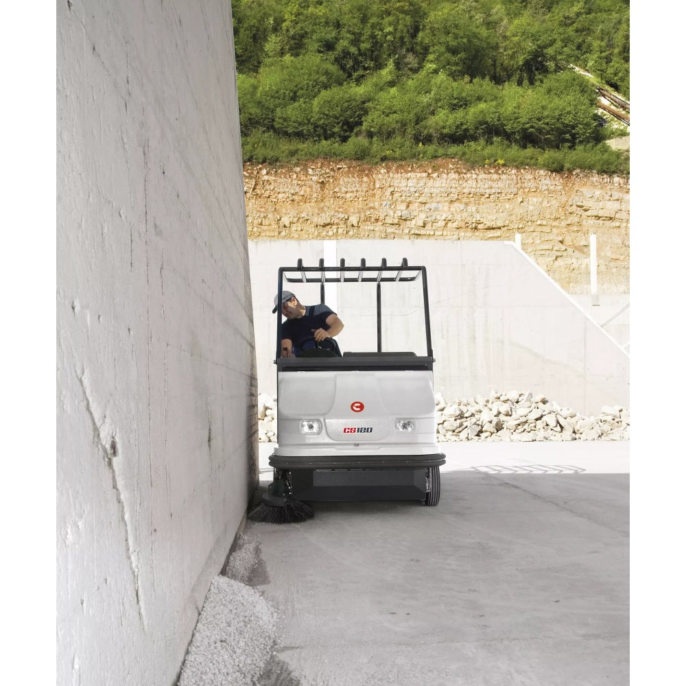 Comac CS120B Ride On Sweeper driving through a narrow alleyway with a person inside