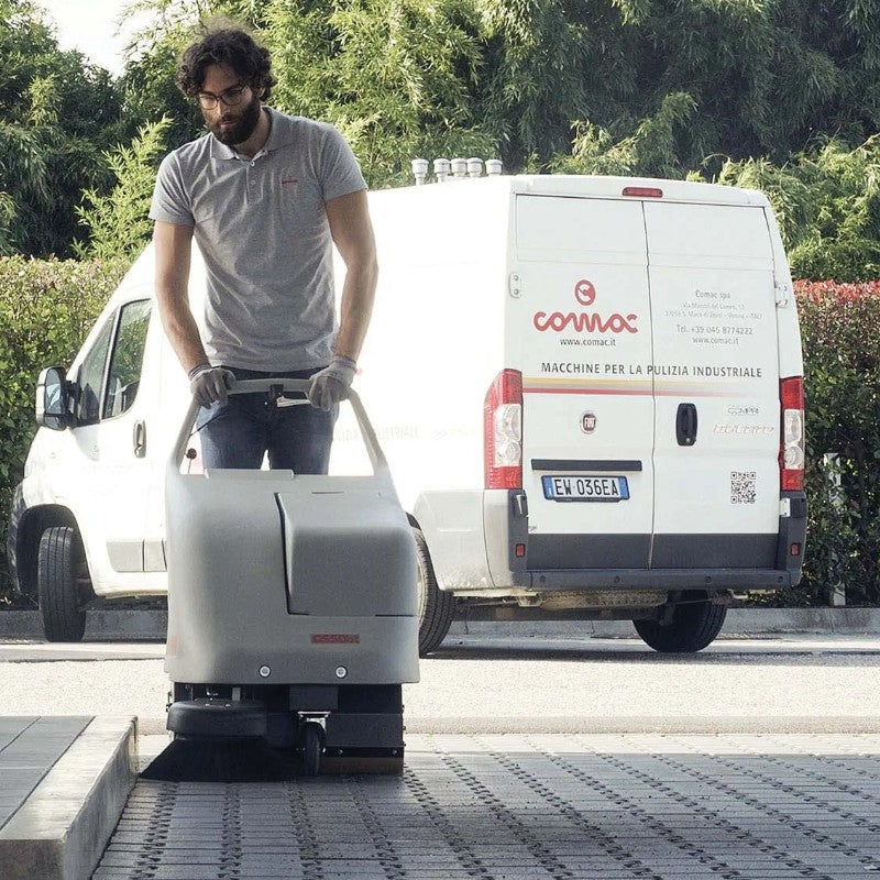Person operating a cleaning machine with a white van in the background
