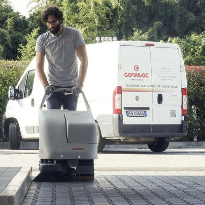 Person operating a cleaning machine with a white van in the background