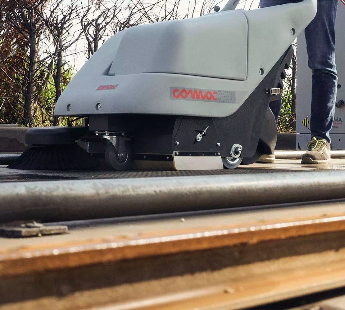 Street cleaning machine with 'COMAC' branding on a road surface.
