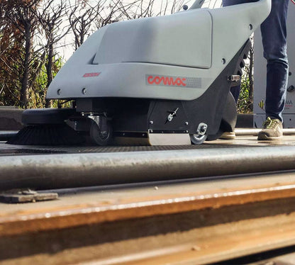 Street cleaning machine with 'COMAC' branding on a road surface.