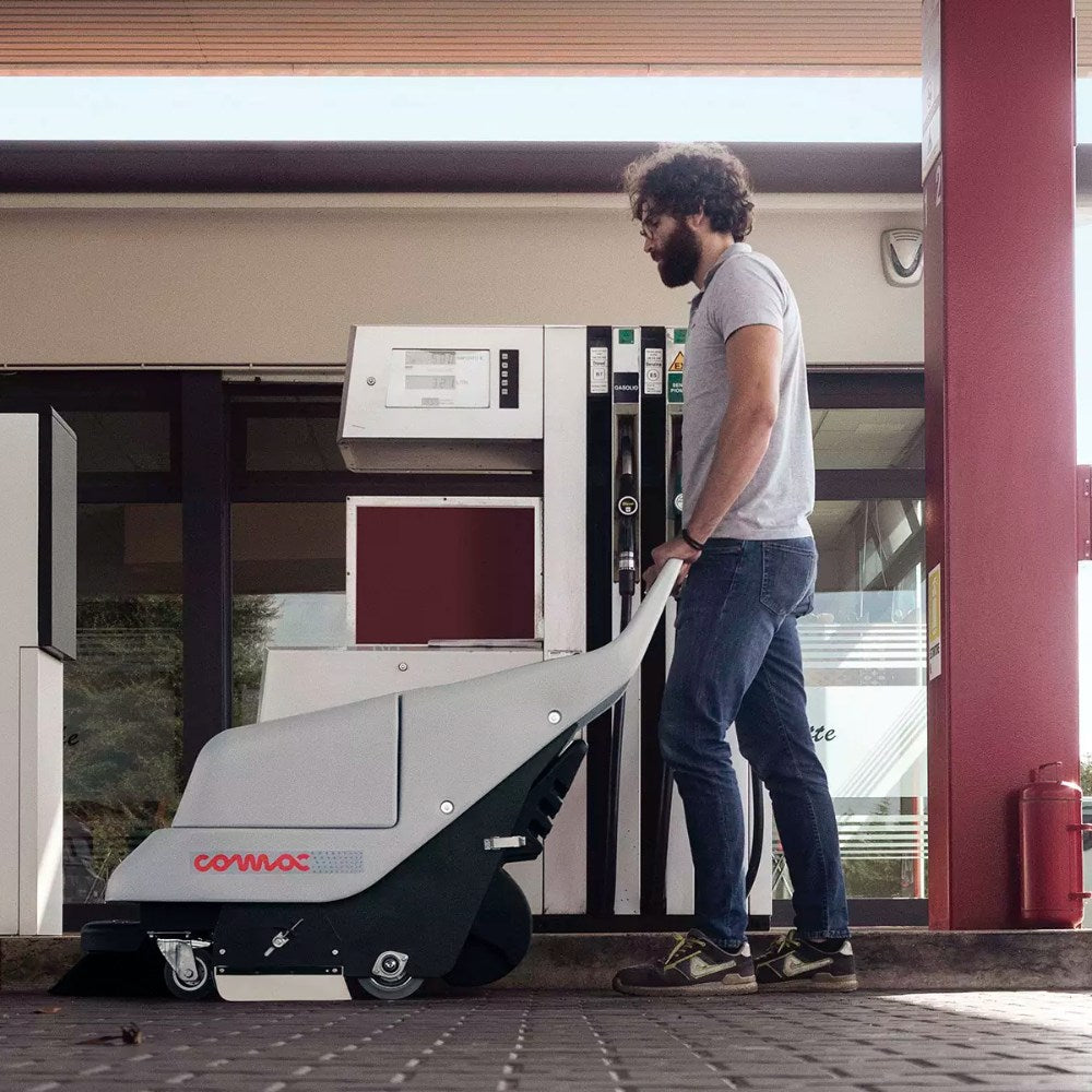 Person using a Comac floor cleaning machine outside a building