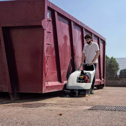 Person operating a Comac scrubbing next to a large red container outdoors.