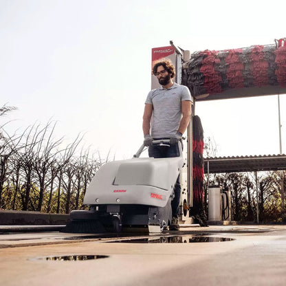 Person operating a floor cleaning machine outdoors with in car wash.