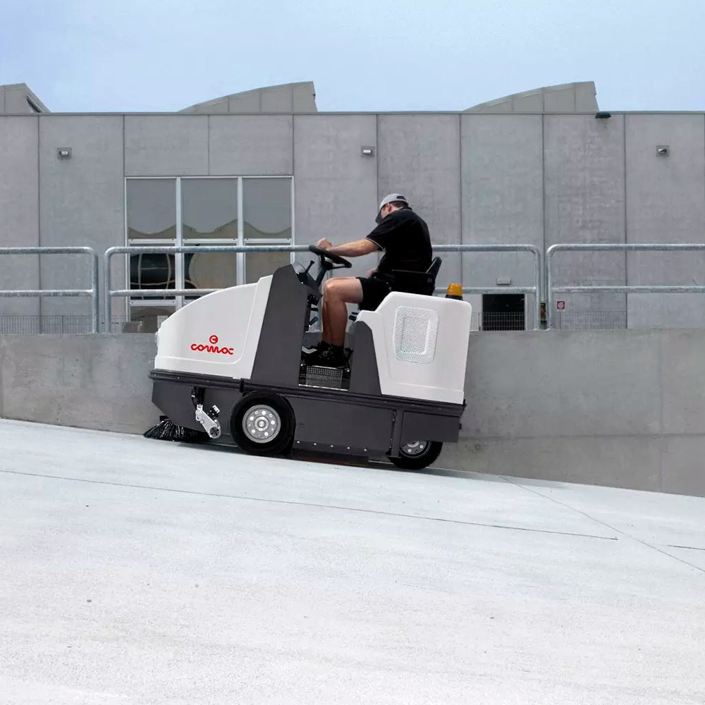 Person operating a Comac Sweeper on an incline with a building in the background