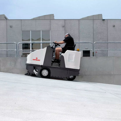 Person operating a Comac Sweeper on an incline with a building in the background
