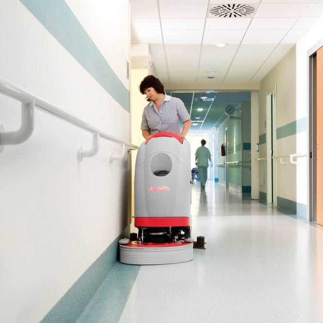 Person operating a floor cleaning robot in a hospital hallway