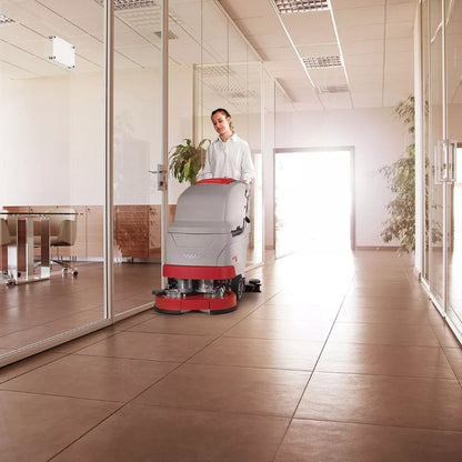 Person operating a floor cleaning machine in a modern office setting