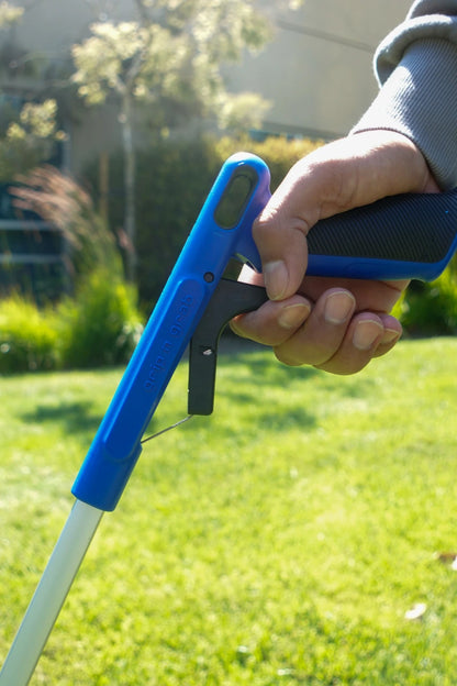 Hand holding a blue and black tool against a grassy background