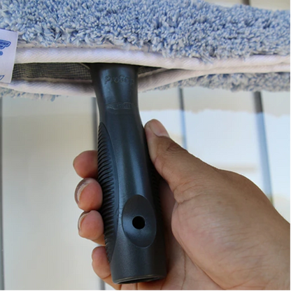 Hand holding a black scrubber with a blue scrubbing pad against a white surface.