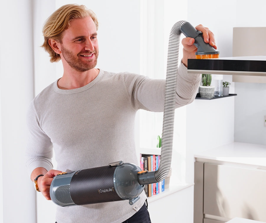 Man using a handheld Halo Capsule Stick Vacuum vacuum cleaner in a modern living room.