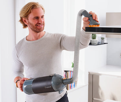 Man using a handheld Halo Capsule Stick Vacuum vacuum cleaner in a modern living room.
