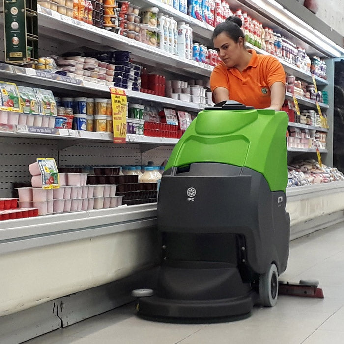 Person operating a green and black IPC CT70 ECS Auto Scrubber machine in a grocery store aisle.