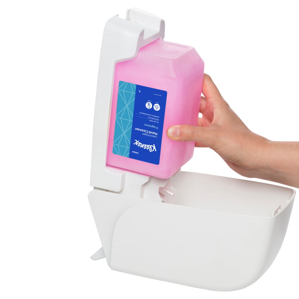 Hand holding a pink container of Kleenex Lux Foam Cleanser over a white dispenser on a white background