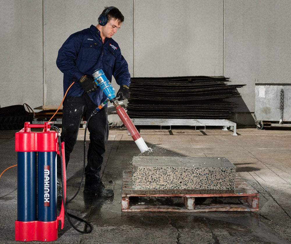 Person using a Makinex Hose 2 Go Water Supply machine on a block of concrete in an industrial setting.