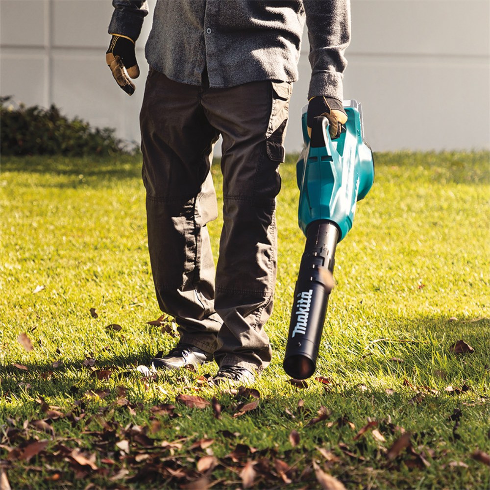 Person holding a Makita leaf blower on a grassy area with scattered leaves.