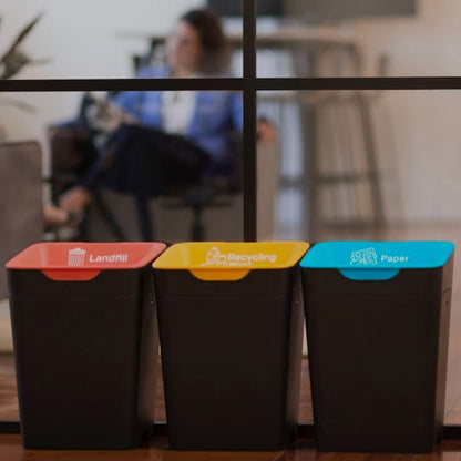 Three recycling bins labeled 'Landfill', 'Recycling', and 'Paper' with a blurred office background.