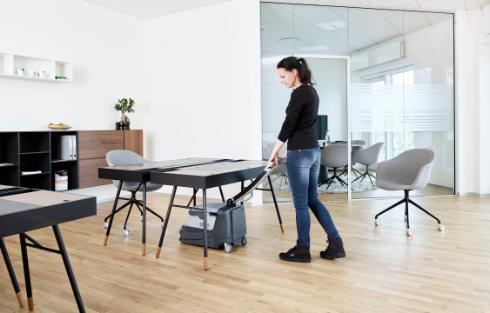 Person cleaning under a table with a Nilfisk SC250 Scrubber in an office setting