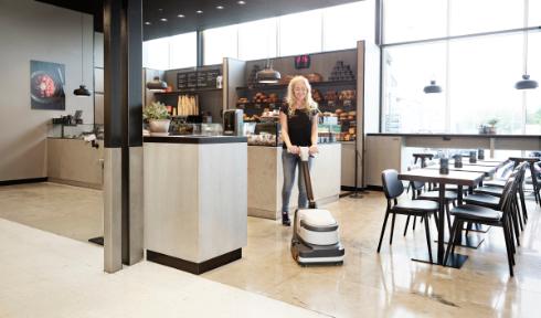 Person using a Nilfisk SC250 Scrubber cleaning machine in a modern kitchen setting
